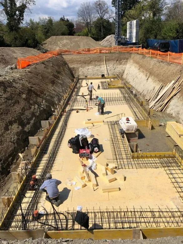Chantier : ouvriers dans une excavation rectangulaire, en train de construire une fondation en béton.