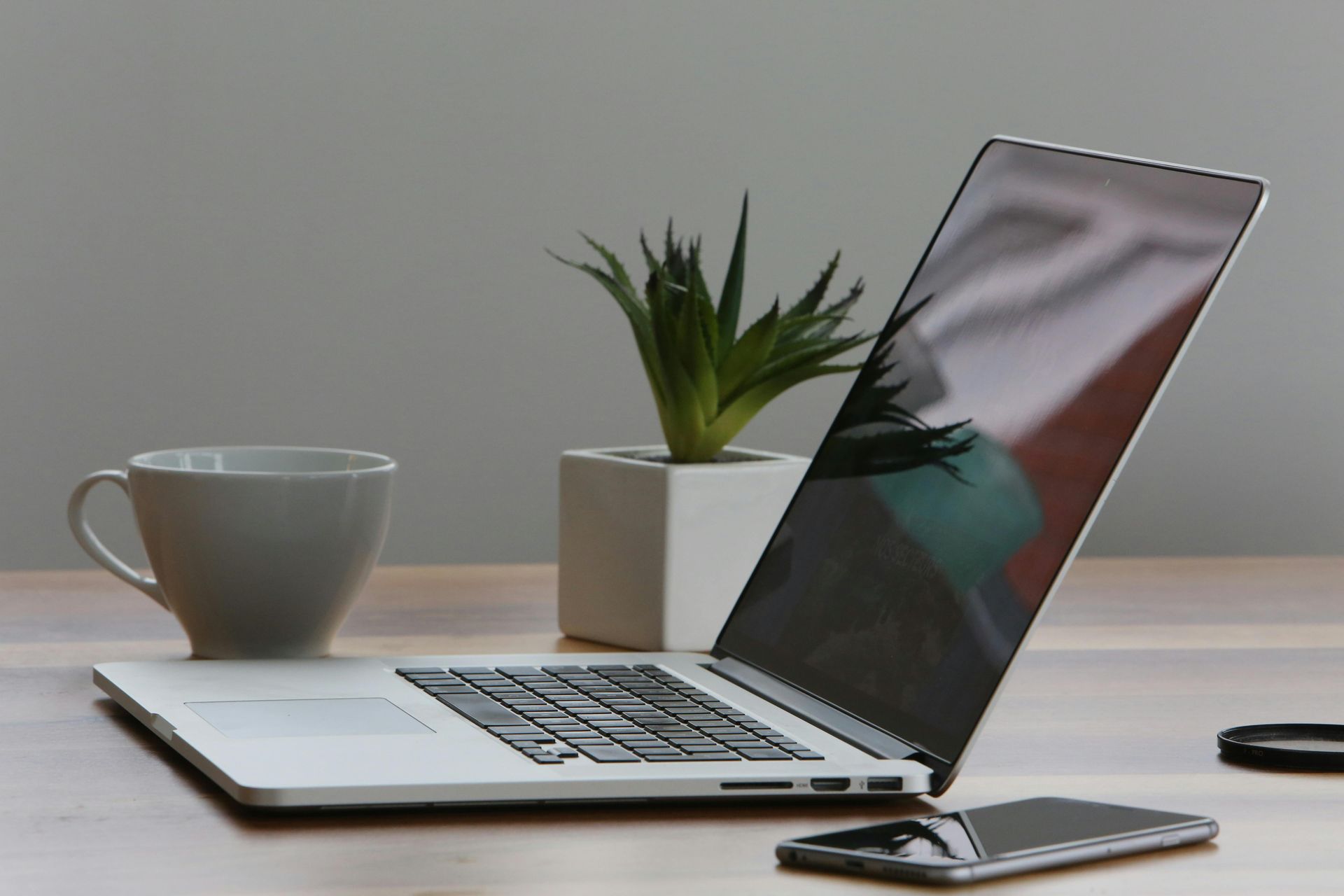 Una computadora portátil está abierta en un escritorio al lado de una taza de café y un teléfono celular.
