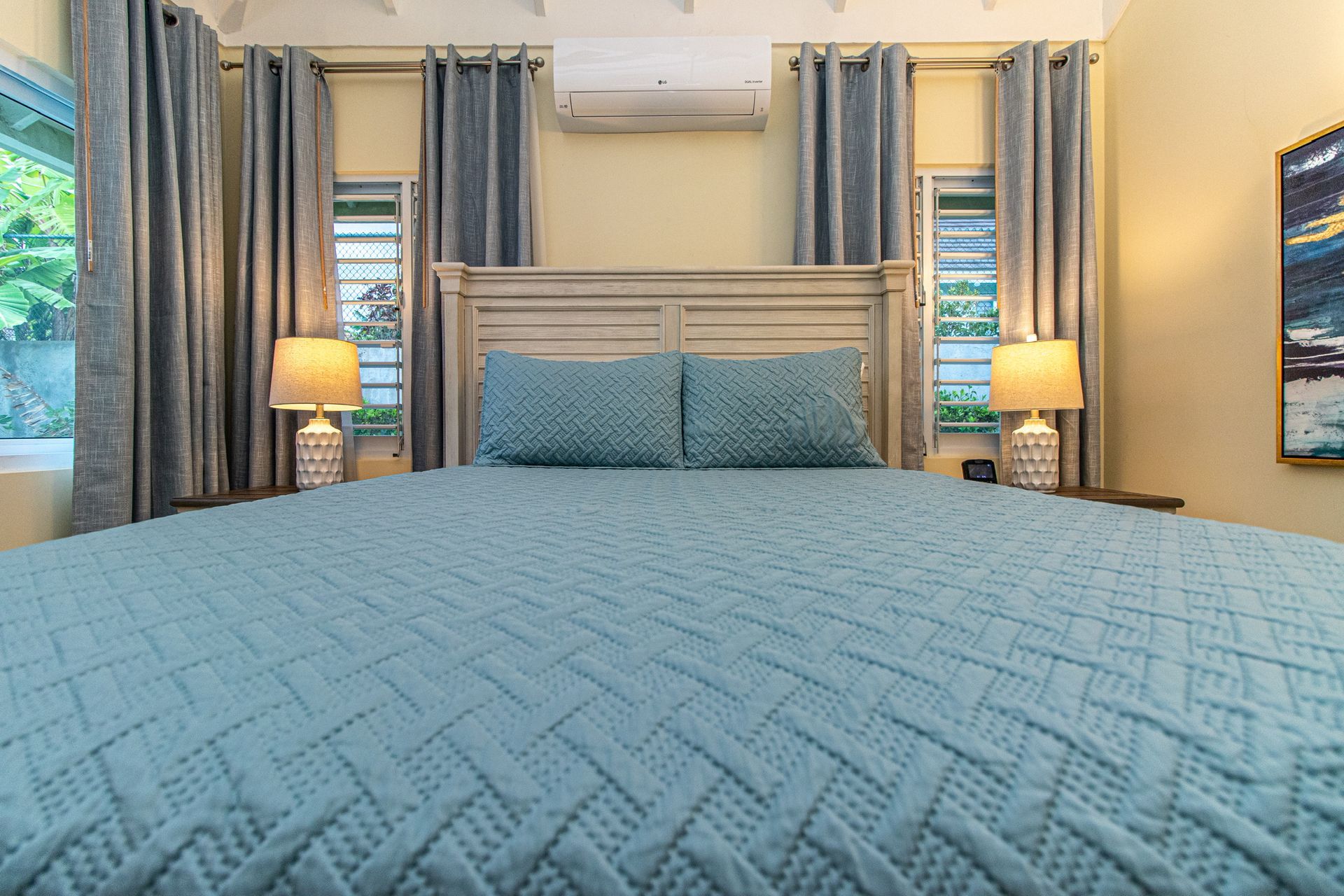 A bedroom with a king size bed , lamps , curtains and a painting on the wall.