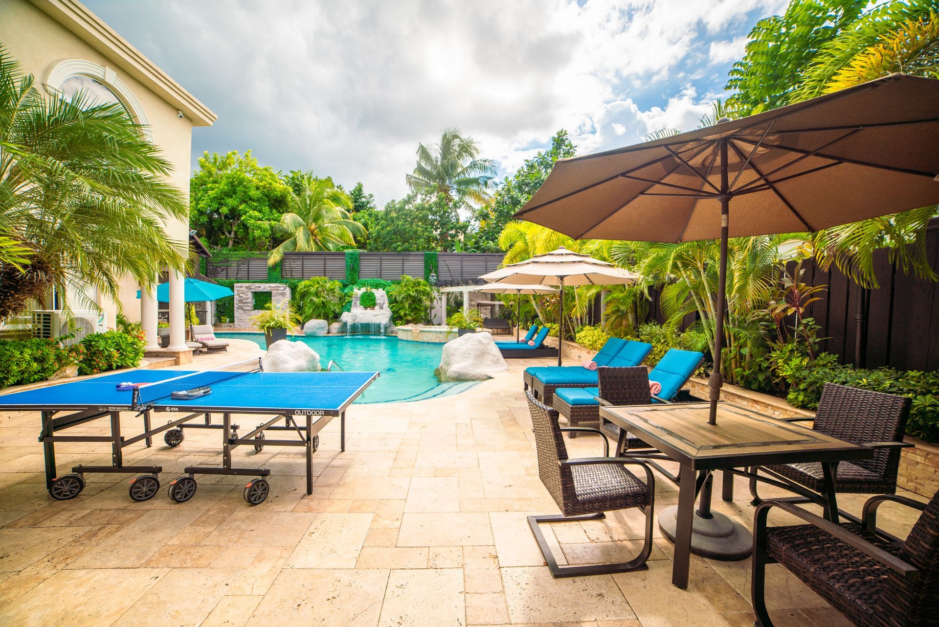 A patio with a table , chairs , umbrellas and a pool.