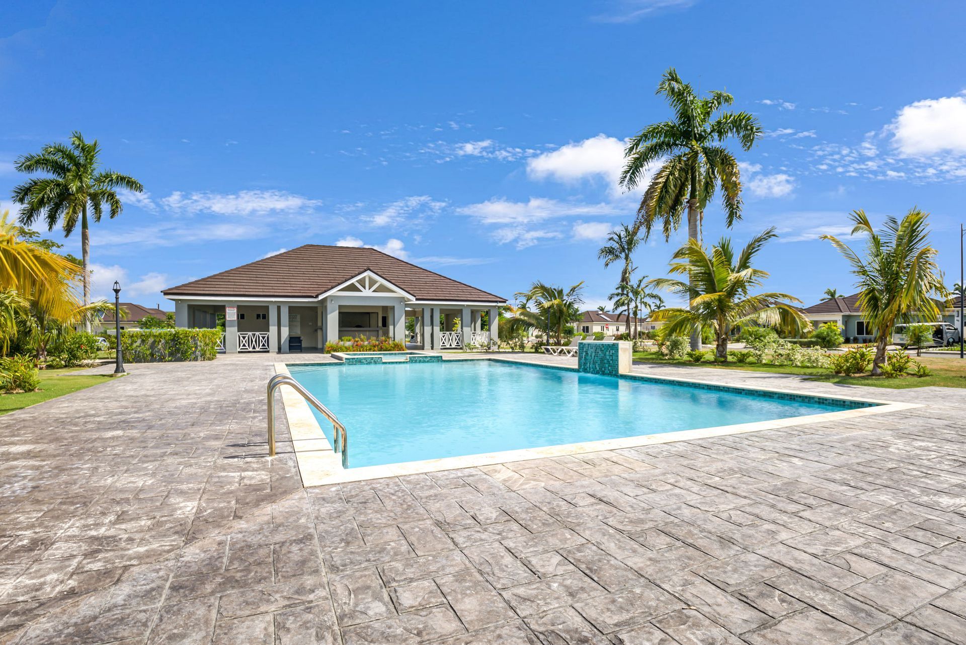 Swimming pool in a tropical setting with palm trees and a clubhouse on a sunny day.