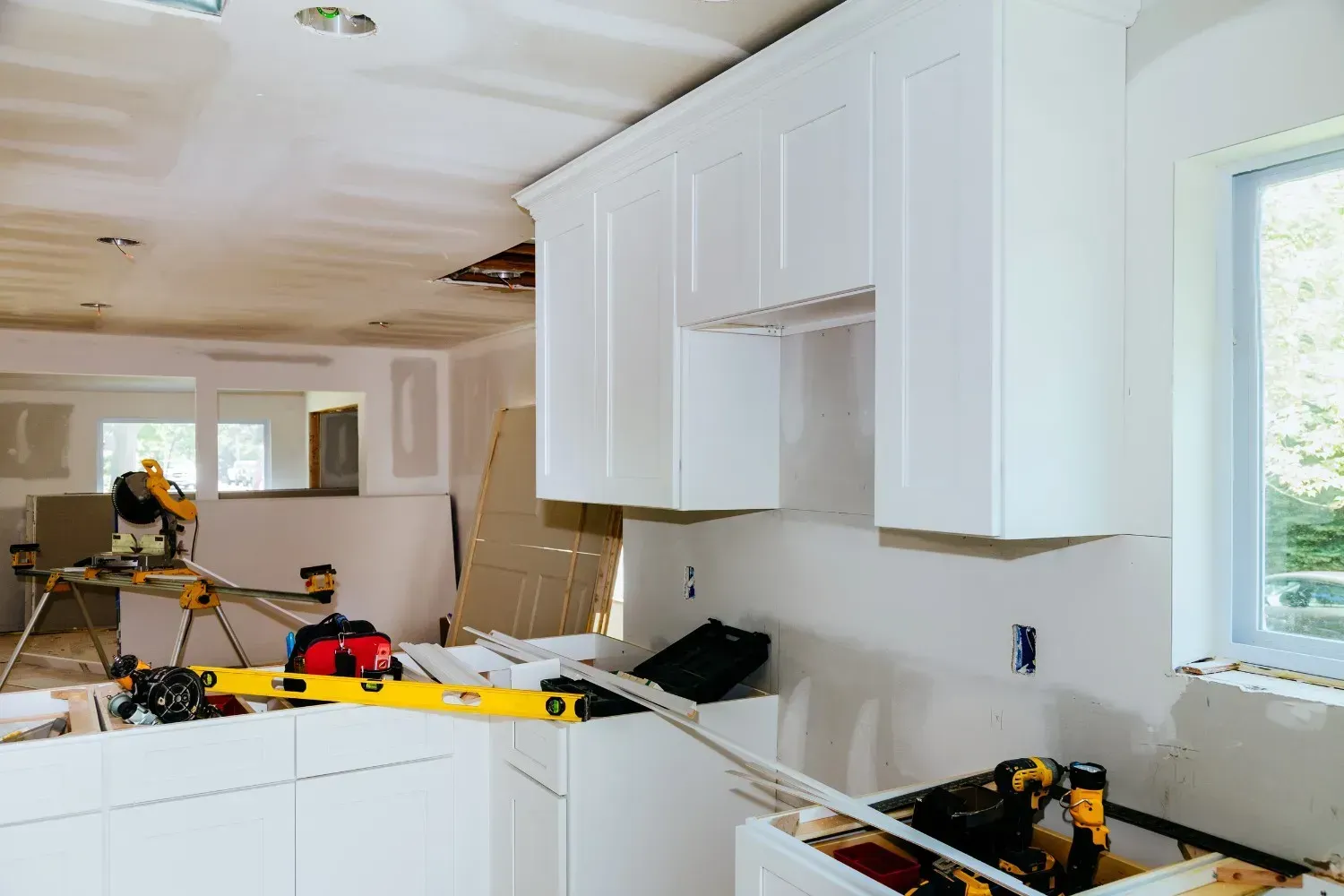 Cocina en proceso de renovación con gabinetes blancos, herramientas y materiales de construcción esparcidos por todas partes.