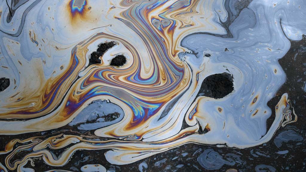 Une nappe d'huile irisée et tourbillonnante sur une surface sombre, affichant un spectre de couleurs.