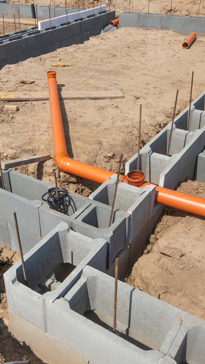 Des tuyaux orange reliés à des blocs de béton, probablement les fondations d'un bâtiment en construction dans une zone sablonneuse.