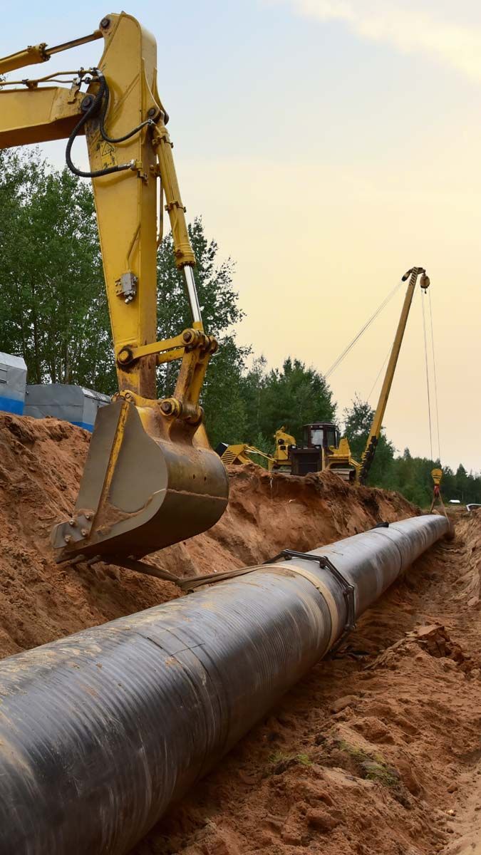 Une pelleteuse jaune enfouit un gros pipeline dans une tranchée.