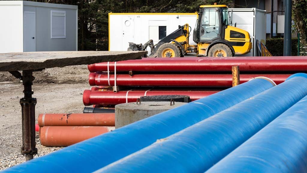 Chantier de construction avec des tuyaux bleus et rouges, une chargeuse jaune et des conteneurs de stockage blancs.
