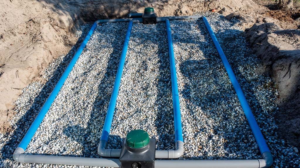 Tuyaux bleus posés sur du gravier dans une zone excavée, faisant partie d'un système septique.