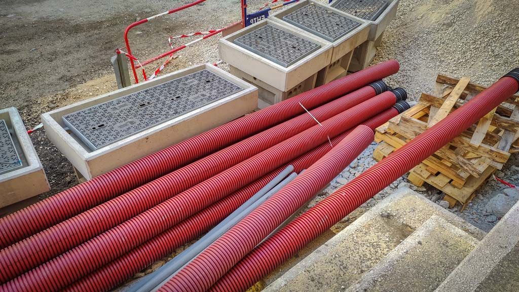 Des tuyaux rouges ondulés sur un chantier, près de conteneurs gris et d'escaliers.
