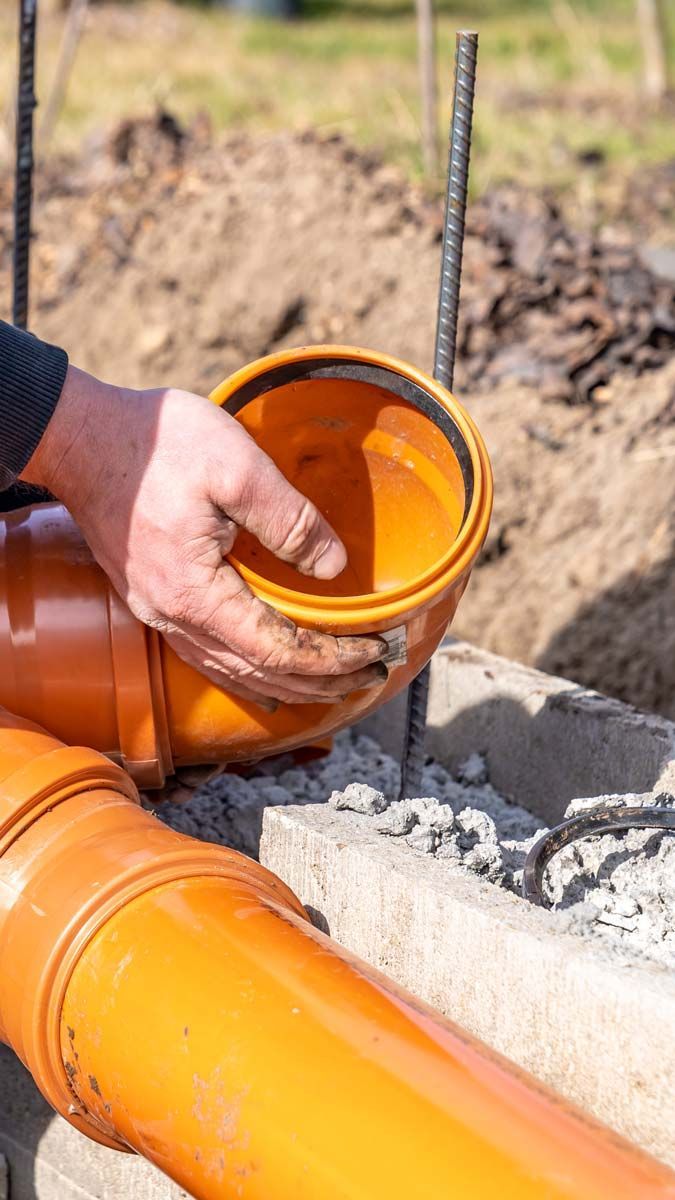 Une personne installe des tuyaux de plomberie en plastique orange avec des raccords à l'extérieur, près d'armatures métalliques.