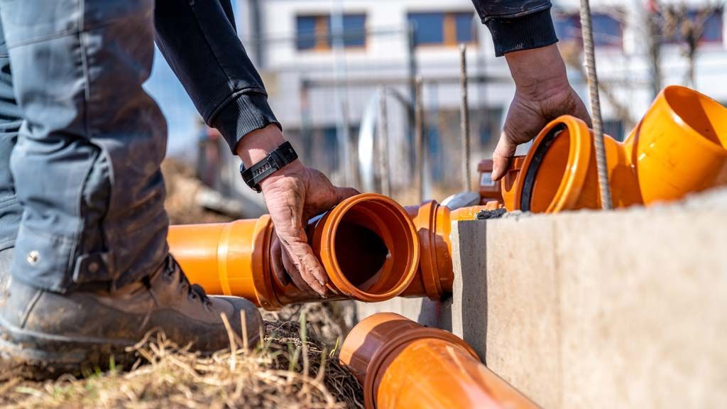 Personne raccordant des tuyaux en plastique orange à l'extérieur.