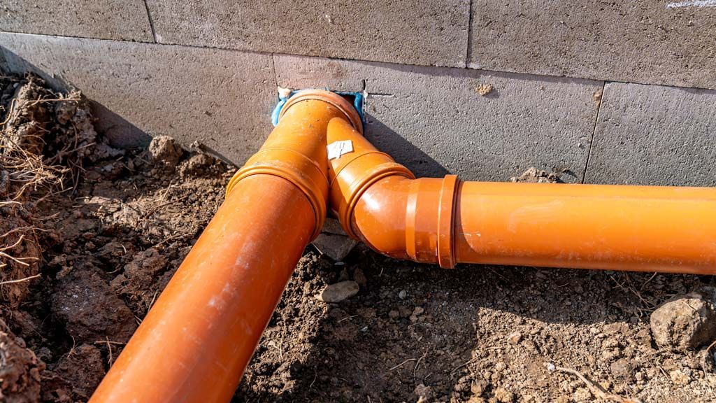 Des tuyaux d'évacuation en PVC orange sont raccordés près d'une fondation en béton.