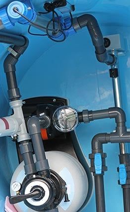Système de filtration de piscine avec tuyaux gris, vannes bleues et manomètre, à l'intérieur d'un boîtier bleu.