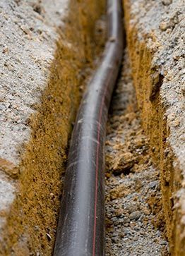 Un tuyau noir dans une tranchée étroite creusée dans le sol, prêt à être enterré.