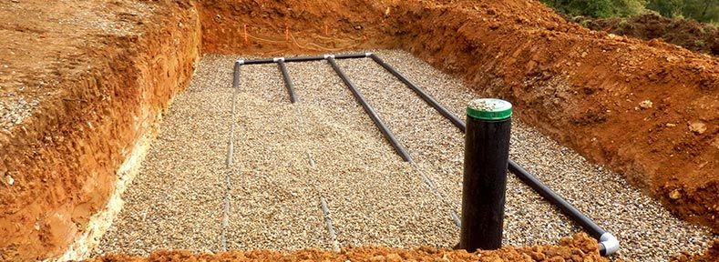 Une fosse creusée avec du gravier, des tuyaux et un tuyau vertical avec un dessus vert.