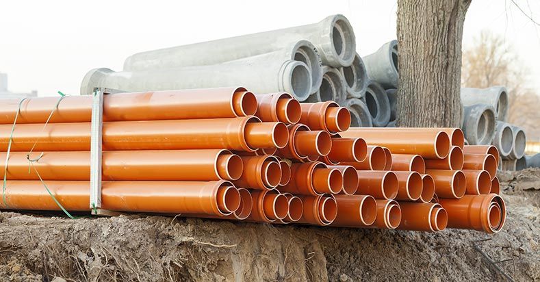 Tuyaux en plastique orange empilés sur la terre, tuyaux en béton gris en arrière-plan.