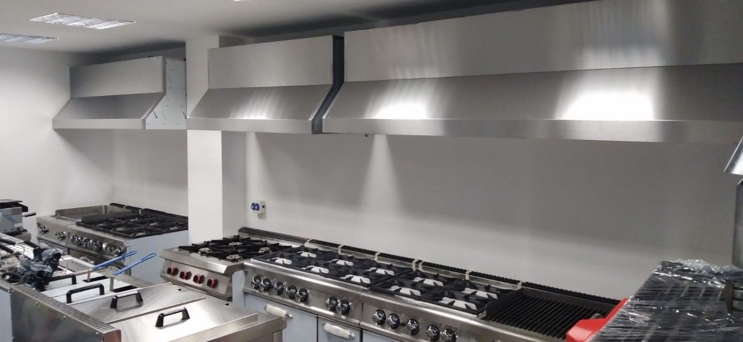 Cocina comercial con estufas, encimeras y grandes campanas extractoras de acero inoxidable.