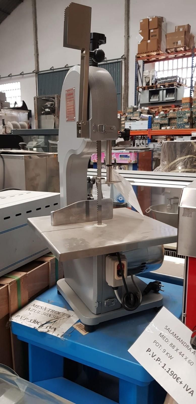 Máquina de coser industrial sobre un banco de trabajo azul en un taller con estanterías y herramientas al fondo.