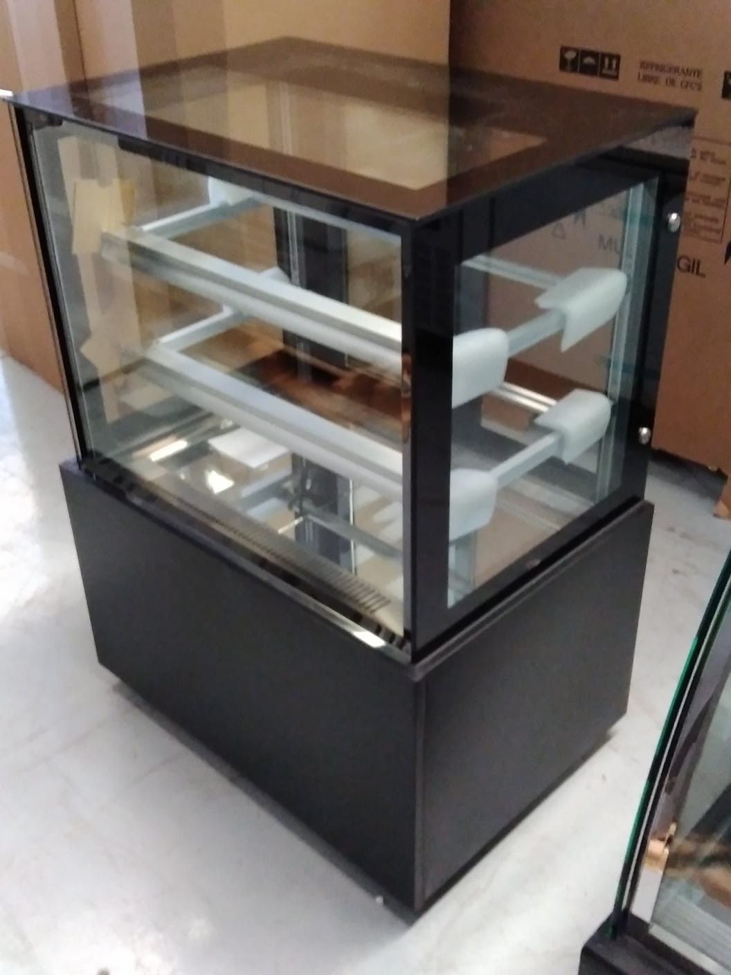 Vitrina de cristal para panadería con estantes blancos vacíos sobre una base negra en un entorno de tienda.