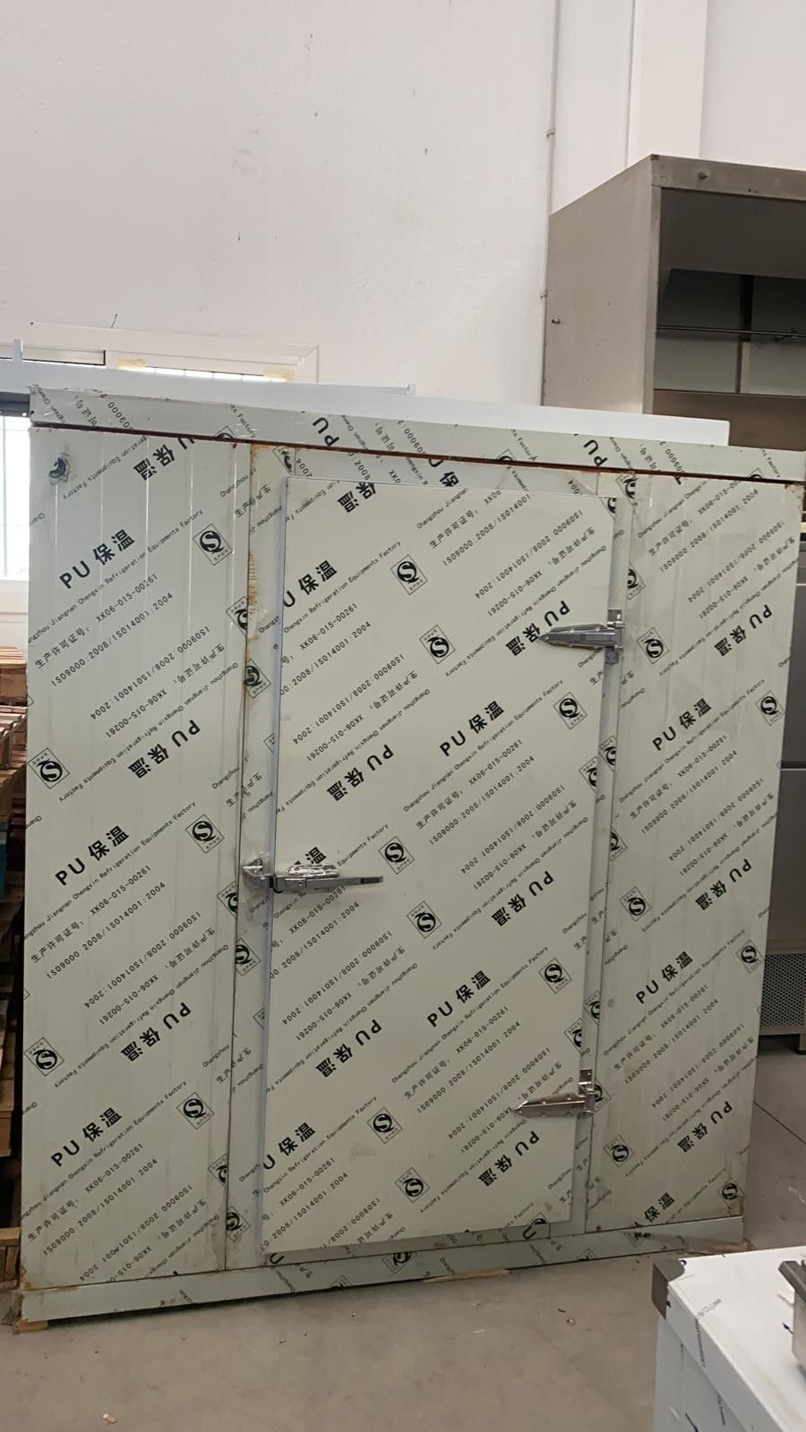 Un gran armario metálico o un frigorífico industrial envuelto en una película protectora, situado en el interior