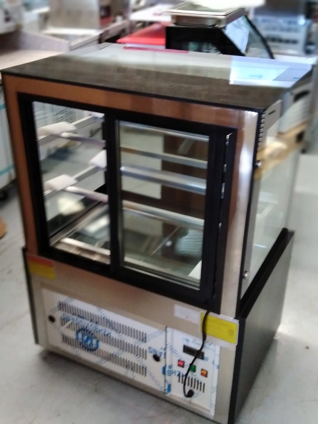 Vitrina de mostrador con frontal de cristal, detalles en negro y tapa metálica, en un entorno comercial.