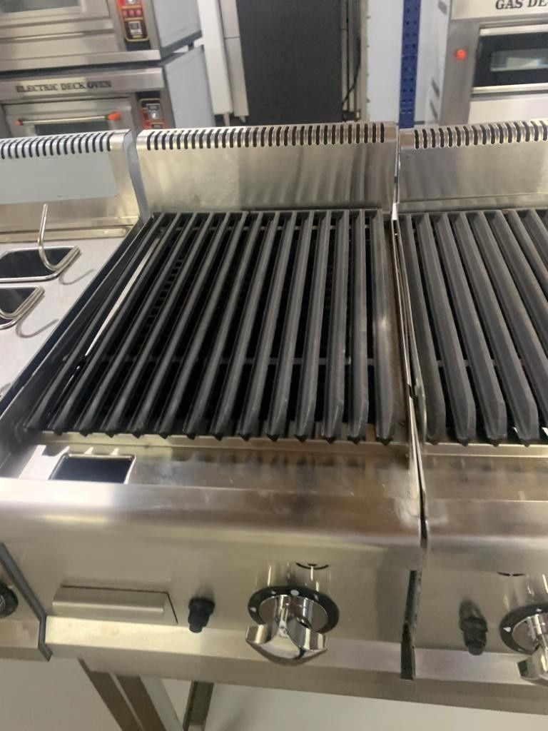 Parrilla comercial de acero inoxidable con filas de brochetas oscuras o quemadores sobre un electrodoméstico