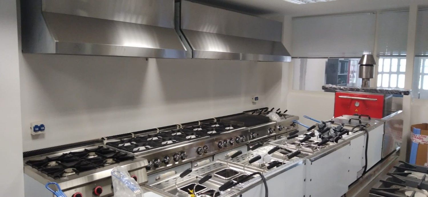 Cocina comercial con encimeras, placas de cocción y grandes campanas extractoras de acero inoxidable.