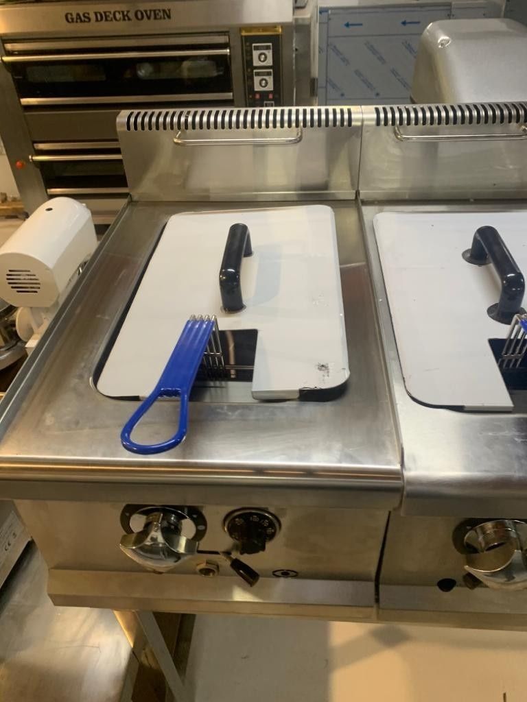 Dos planchas eléctricas con asas negras sobre una encimera de acero inoxidable en una cocina comercial.