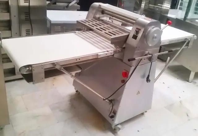 Máquina transportadora industrial con cinta blanca y rodillos metálicos en un taller.