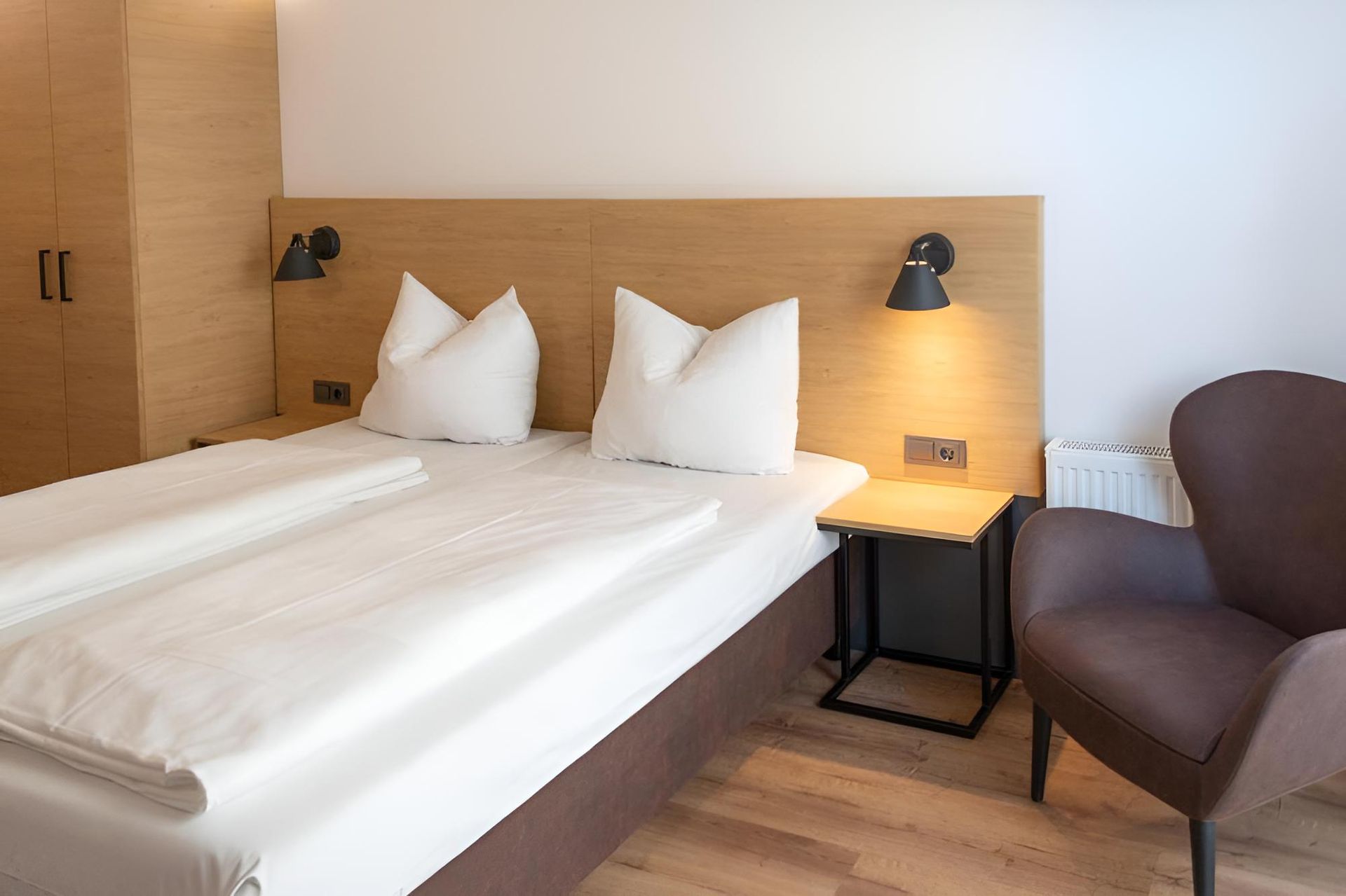 Geräumiges Zimmer mit modernem Mobiliar, Twin-Boxspringbett, Esstisch, Sofa, Relaxsessel, Flachbild-TV und Vinylboden.