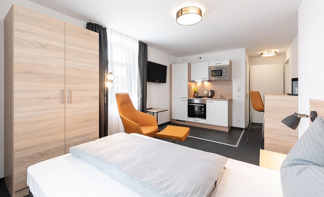 Geräumiges Hotelzimmer mit modernem Mobiliar, Boxsspringbett Einzelbett und Küche, Sitzgelegenheit und Kleiderbügel  im Apartmenthotel Apartimo Landshut.