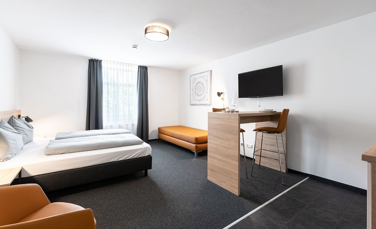Geräumiges Hotelzimmer mit modernem Mobiliar, TwinBoxsspringbett,  Essenstisch, Sofa, Relaxsessel, Flachbild-TV und Vinylboden im Apartmenthotel Apartimo Landshut.