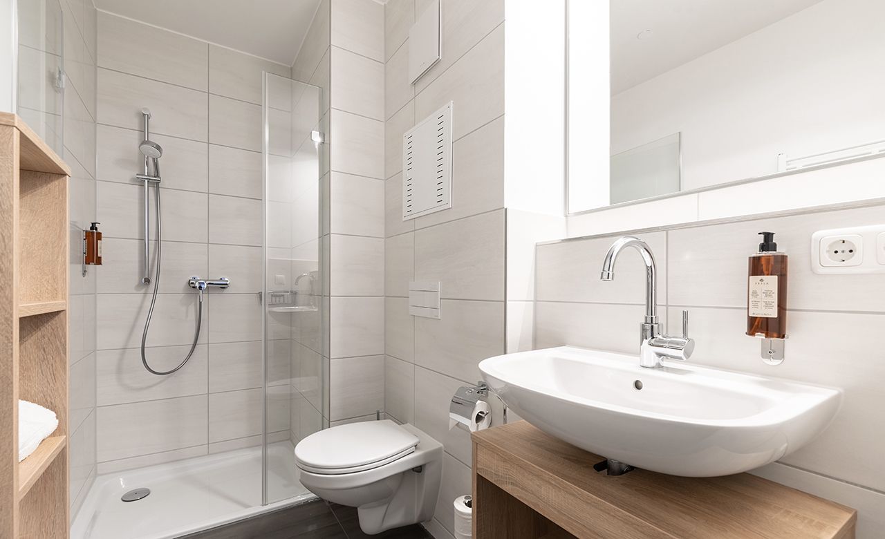 Ein privates modernes Badezimmer mit Toilette , Waschbecken und Dusche,Haartrockner, Duschgel und Shampoo und Handtücher im Apartmenthotel Apartimo Landshut