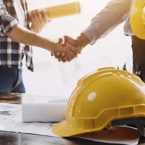 Dos hombres se dan la mano delante de un casco amarillo.