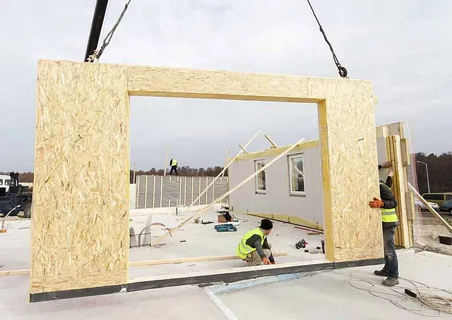 Una grúa está levantando una pared de madera en un edificio en construcción.
