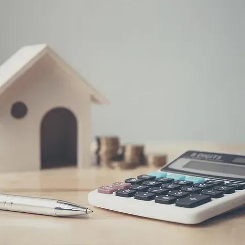 Una calculadora está sobre una mesa al lado de un bolígrafo y una maqueta de casa.