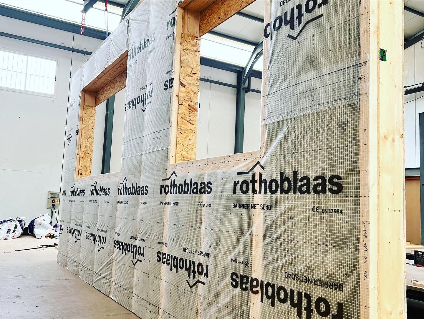 Estructura de edificio de madera con aberturas para ventanas, recubierta con un film de la marca 