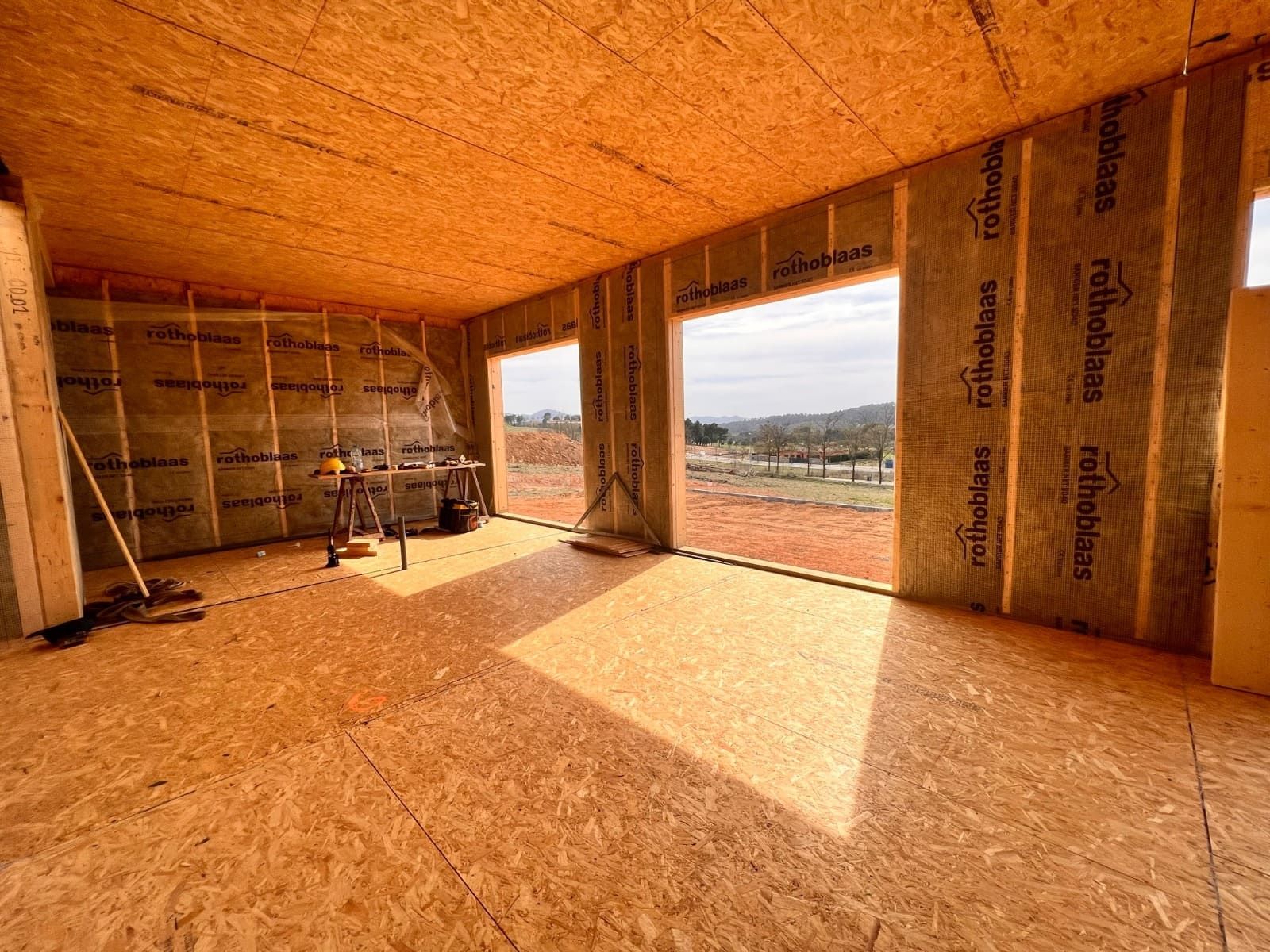 Vista interior de un edificio en construcción, suelo y paredes de OSB, aislamiento visible, dos puertas.