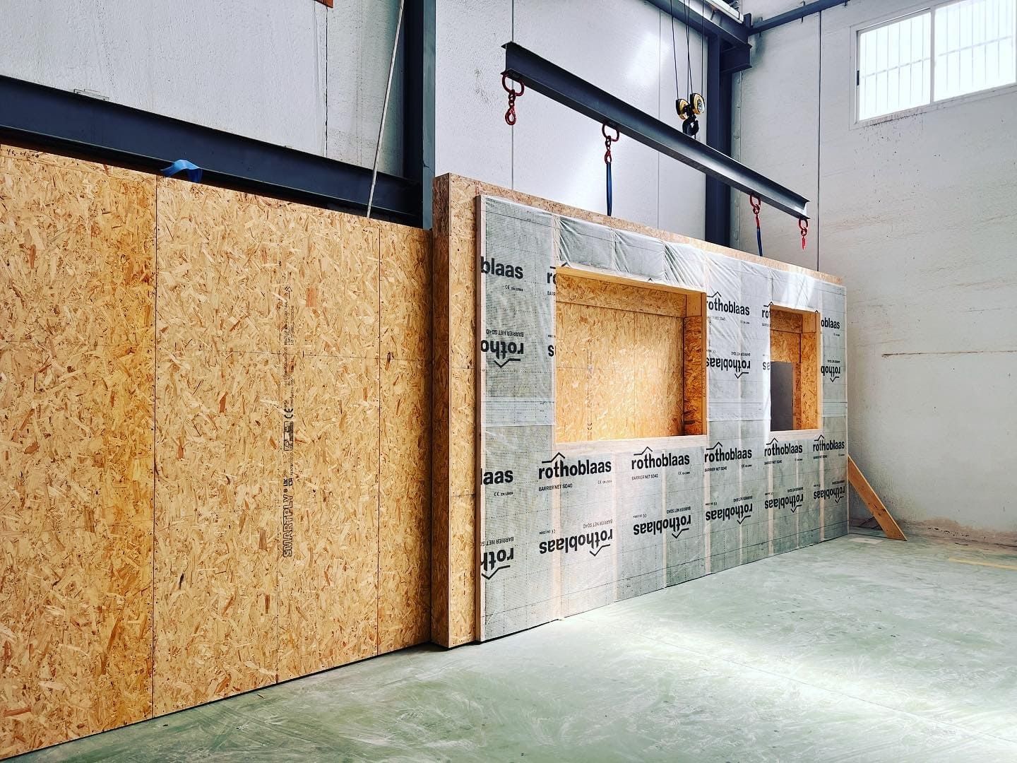 Obra: Paneles de pared de madera, uno de ellos con recortes para ventanas, suspendidos por una grúa.