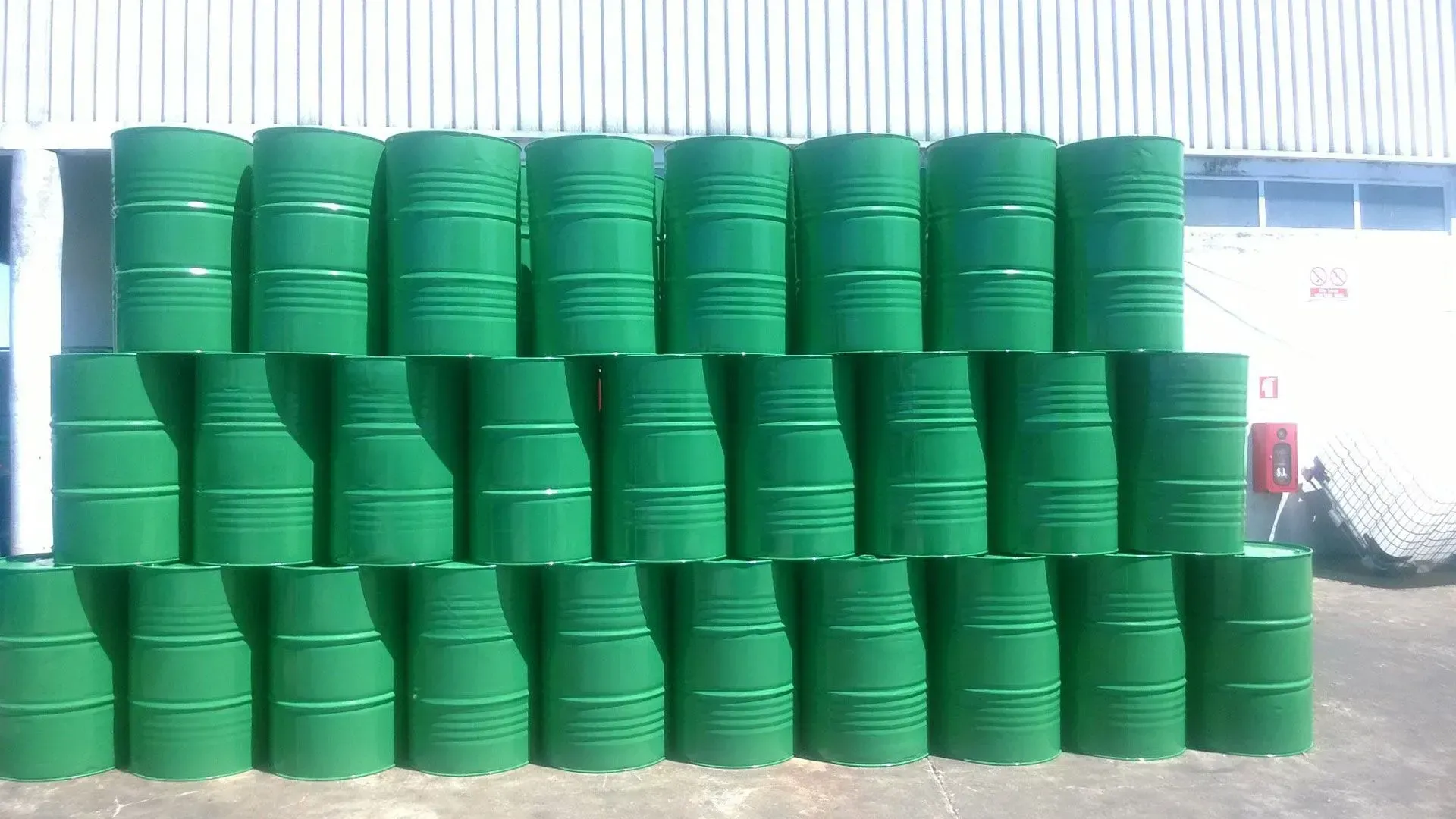 Um monte de barris verdes empilhados uns sobre os outros em frente a um prédio.