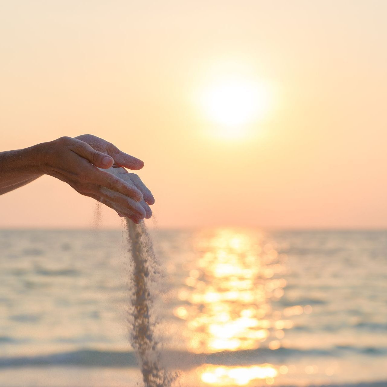 Mains qui vident du sable avec un coucher de soleil