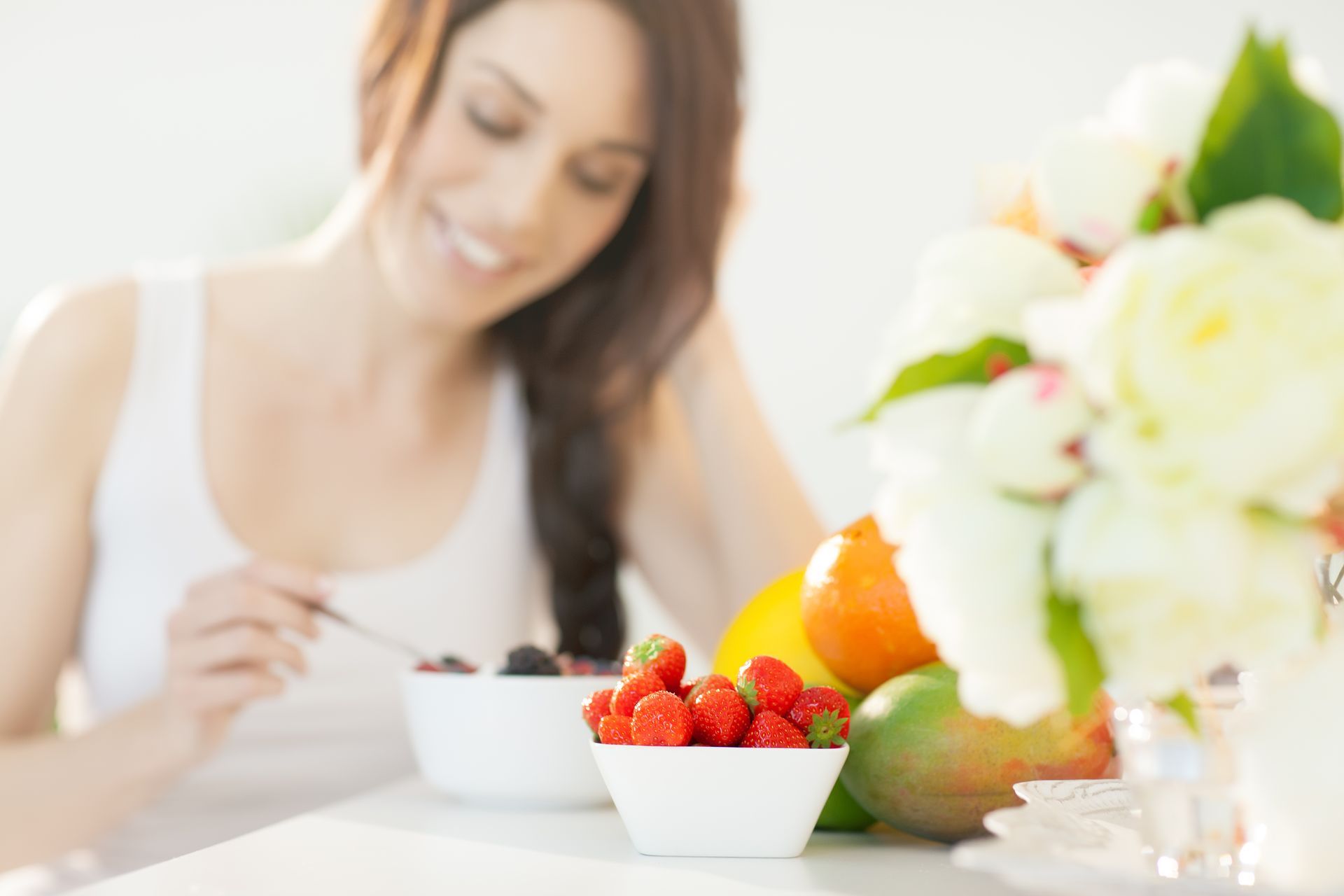Una mujer está sentada en una mesa comiendo un tazón de fruta.