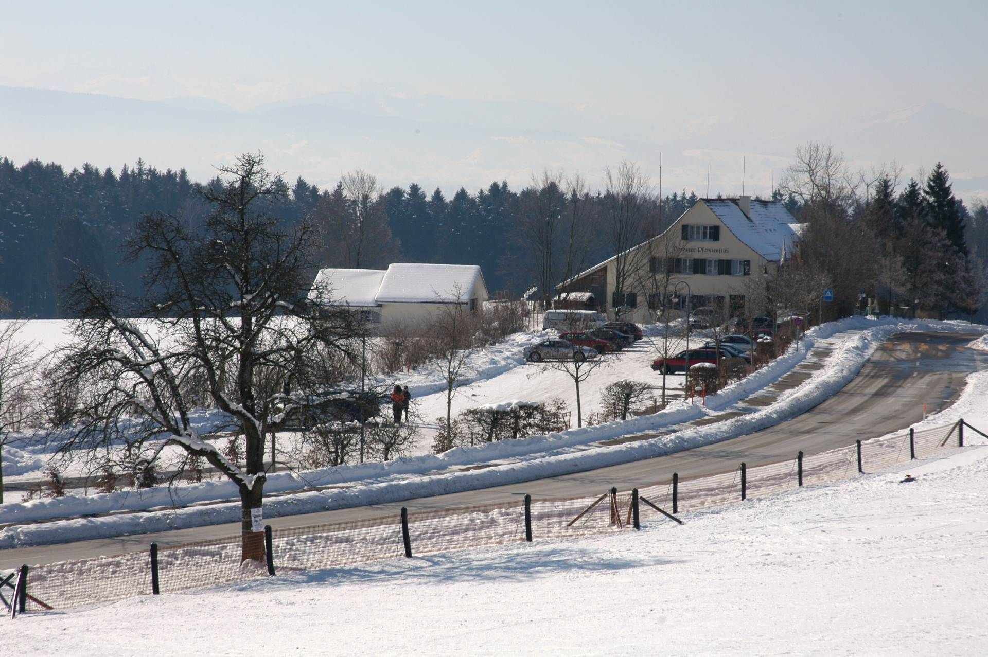 Eine verschneite Strasse mit einem Gebäude im Hintergrund. Foto von der Restaurant Pfannenstiel AG