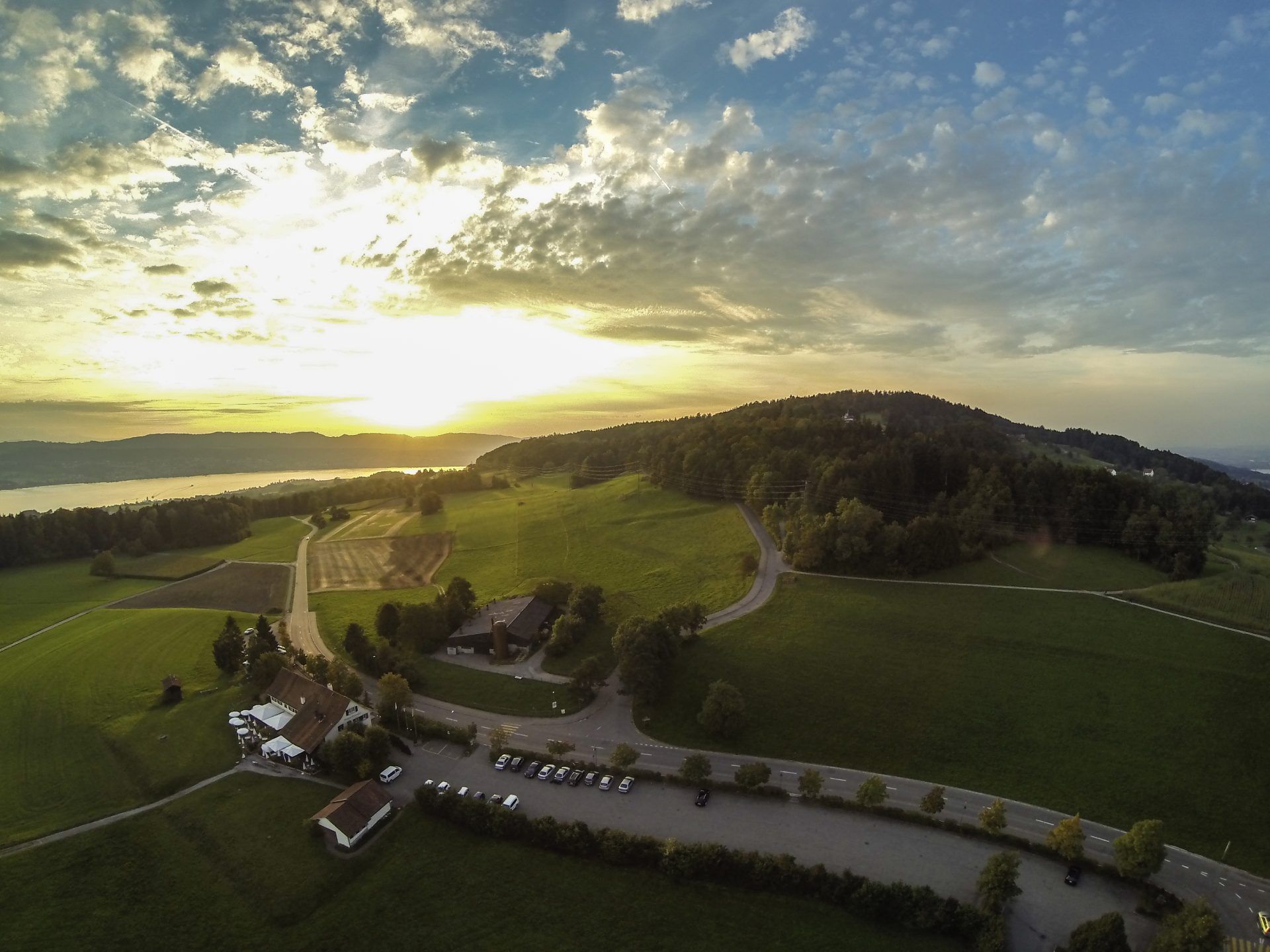 Luftaufnahme eines Feldes bei Sonnenuntergang mit einem See im Hintergrund. Foto von der Restaurant Pfannenstiel AG.