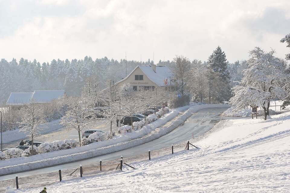 Eine verschneite Strasse mit einem Gebäude im Hintergrund. Foto von der Restaurant Pfannenstiel AG.