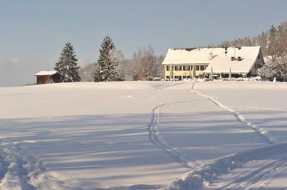 Ein schneebedecktes Feld mit einem Gebäude im Hintergrund. Foto von der Restaurant Pfannenstiel AG.