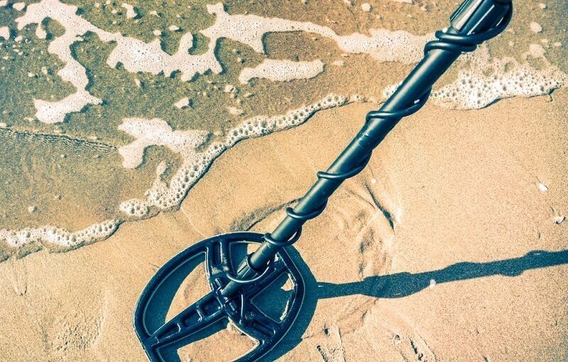 A metal detector is sitting in the sand on the beach.