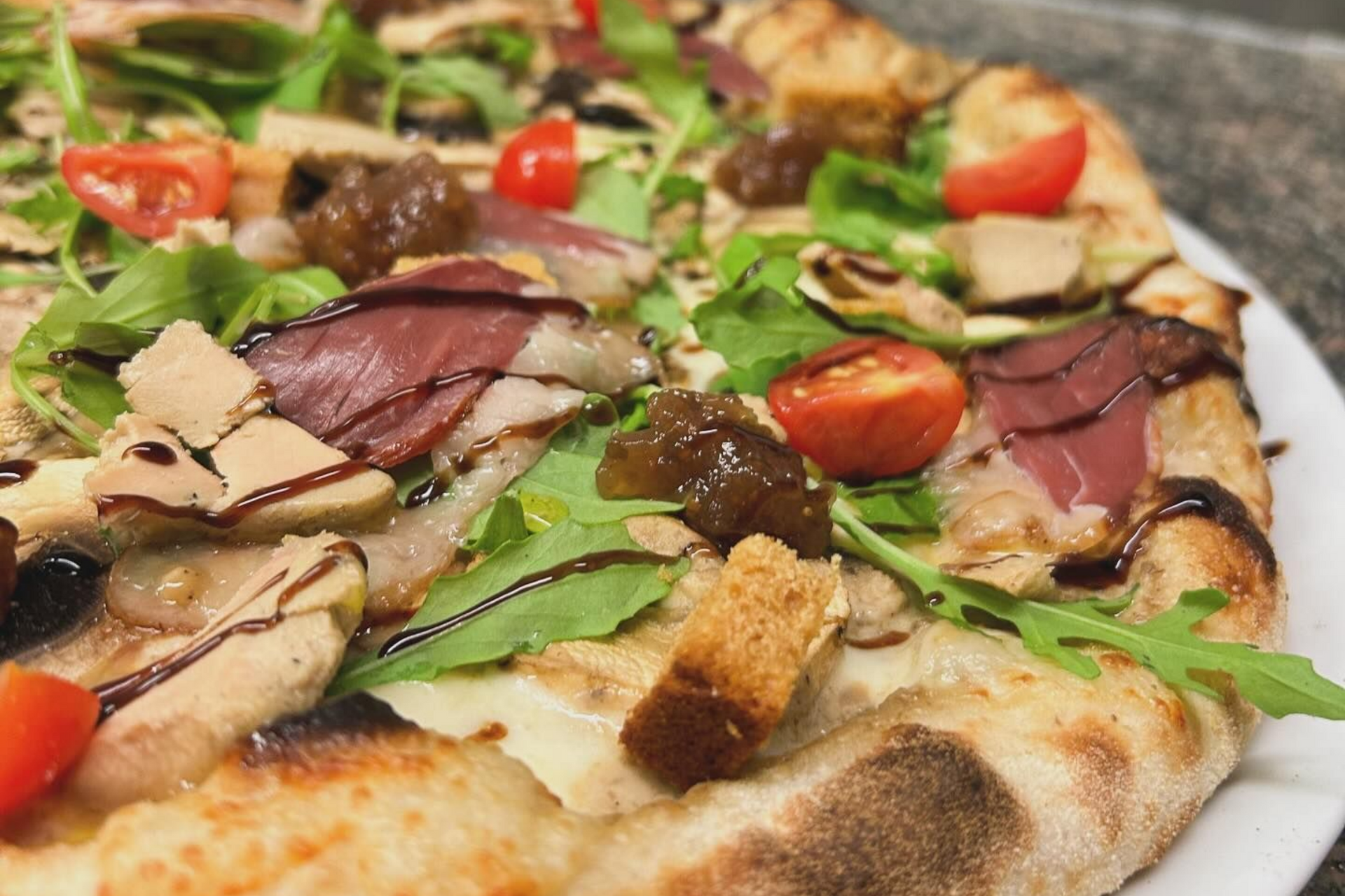 Une pizza garnie de jambon cru, tomates et roquette.