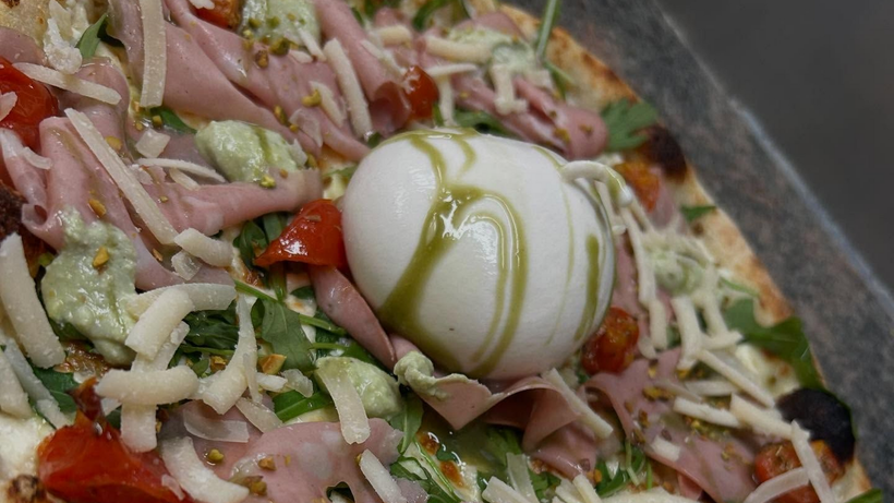 Une pizza garnie d'une burrata avec du jambon.
