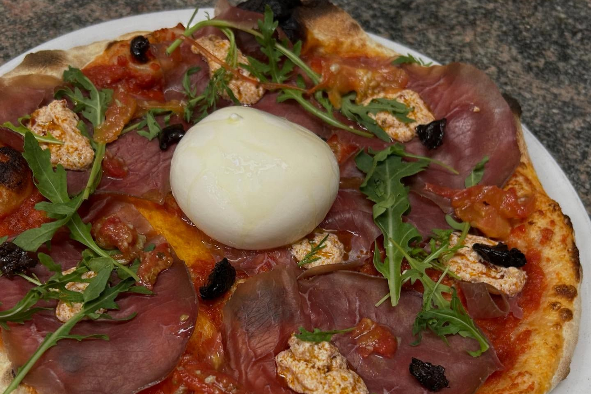 Une pizza garnie d'une burrata et de jambon cru.