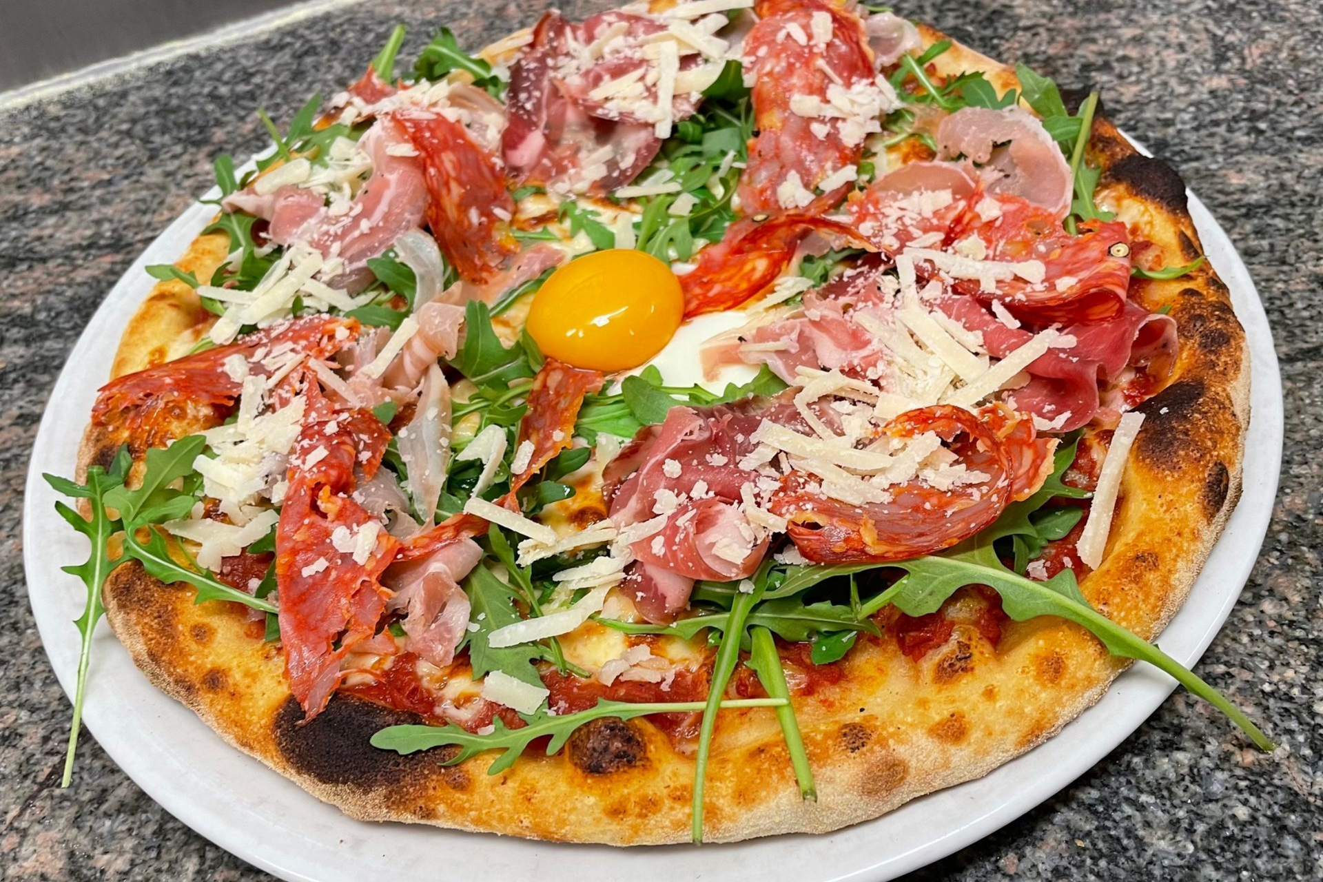 Une pizza garnie de charcuterie et d'un œuf cru.